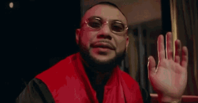 a man with a beard wearing sunglasses and a red jacket is sitting in front of a window .