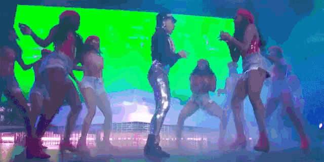a group of dancers are dancing on a stage in front of a green screen .