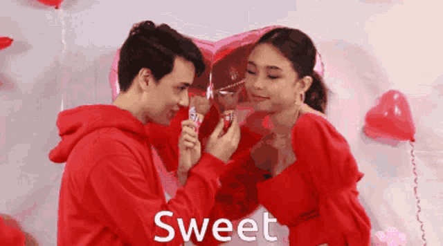 a man and a woman are standing in front of a heart shaped balloon with the word sweet on the bottom