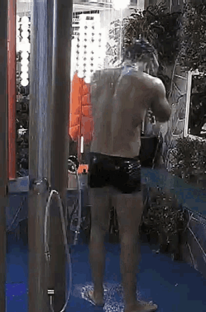 a man without a shirt is taking a shower in a outdoor shower .