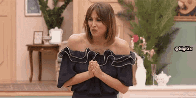 a woman wearing a blue off the shoulder top is standing in a room with her hands folded .