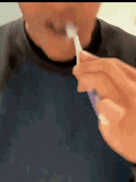a man in a blue shirt is brushing his teeth with a purple toothbrush