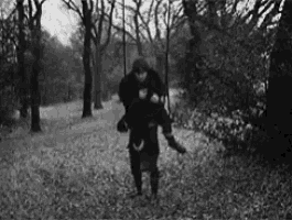 a black and white photo of a man carrying a woman on his back in a park .