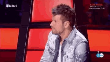 a man in a denim jacket is sitting in a chair with a red seat cushion .