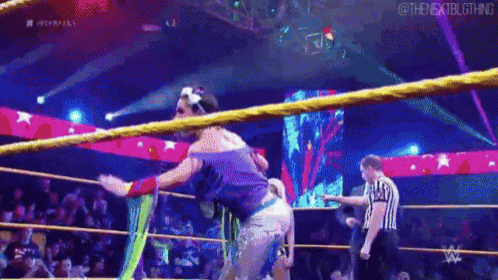 a woman is standing in a wrestling ring with a referee standing behind her .