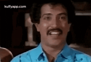 a man with a mustache wearing a blue shirt is smiling .