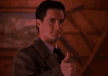 a man wearing a suit and tie is giving a thumbs up .