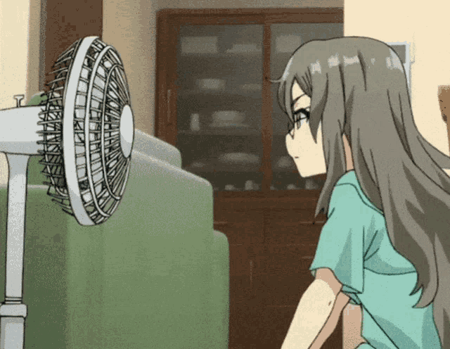 a girl in a green shirt is looking at a fan in a living room