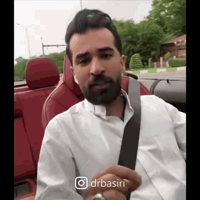 a man with a beard is sitting in a red car with a belt around his waist