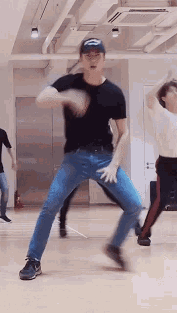 a man in a black shirt and blue jeans is dancing in a room with other people .