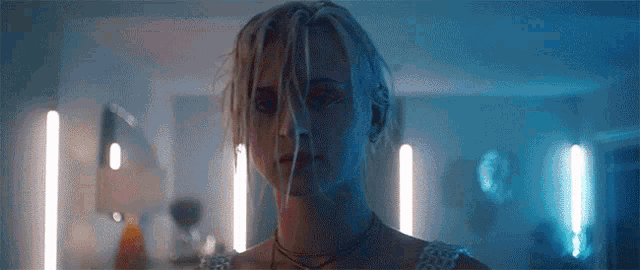 a woman with dreadlocks is standing in a dark room with blue lights behind her .
