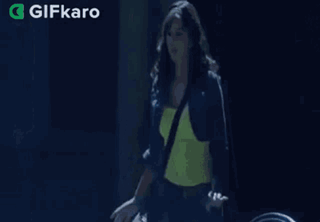 a woman in a blue jacket and a neon yellow top is dancing in the dark .