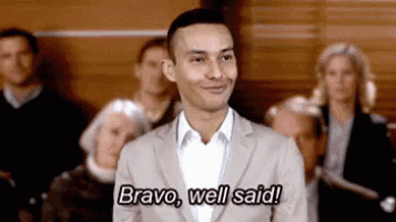 a man in a suit is standing in front of a crowd of people and saying `` bravo , well said '' .