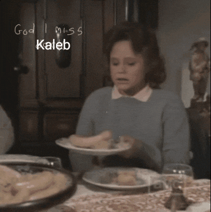a woman sits at a table with a plate of food and the words god i miss kaleb written on the wall behind her