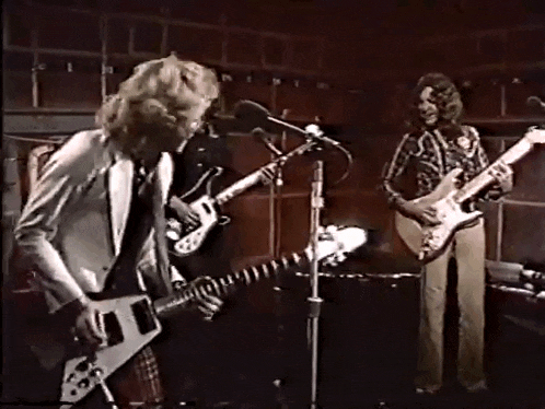 two men playing guitars and singing into microphones on stage