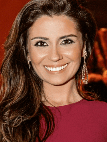 a woman wearing a pink top and earrings smiles