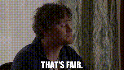 a man with curly hair is sitting at a table with the words `` that 's fair '' written on his face .