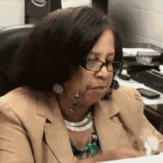 a woman wearing glasses and a necklace is sitting at a desk in an office .