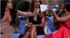 three women are sitting on a blue couch and one of them is holding a megaphone .