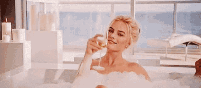 a woman is taking a bath in a tub while holding a glass of champagne .