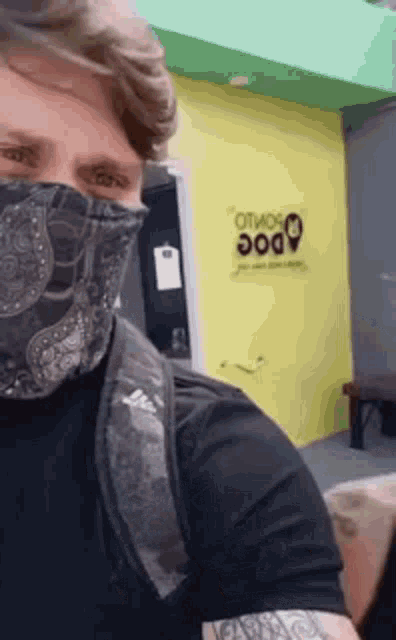 a man wearing a bandana around his face is standing in front of a yellow wall that says dog