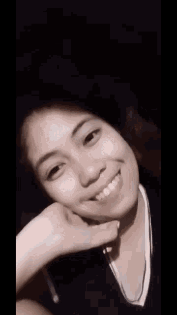a close up of a woman 's face with her hand on her chin and smiling .
