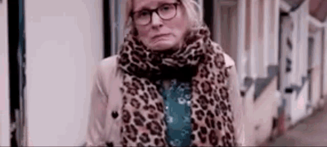 a woman wearing glasses and a leopard print scarf is standing on a street .