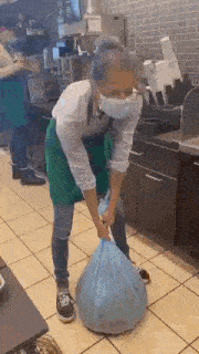 a woman wearing a mask is carrying a large bag of trash in a kitchen .