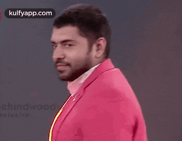a man in a pink jacket is making a funny face while holding his hand to his chin .