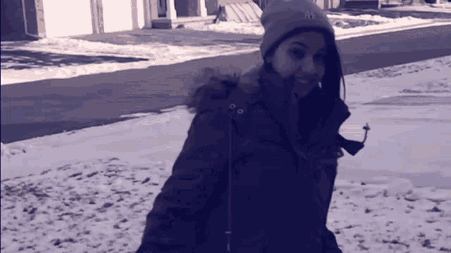 a woman wearing a ny hat and a parka is walking in the snow