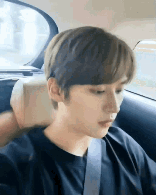 a young man is sitting in the back seat of a car wearing a black shirt and a seat belt .