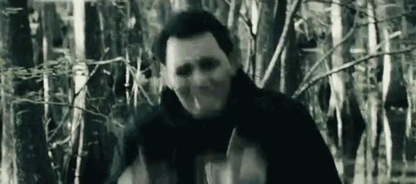 a man with a scarf around his neck is standing in the woods .