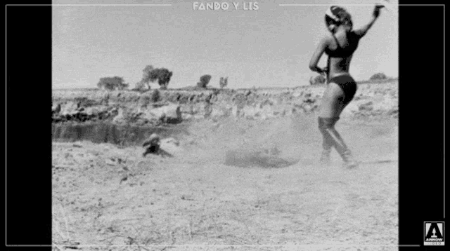 a black and white photo of a woman in a bikini standing in the dirt