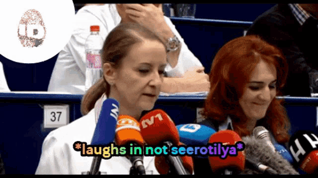 a woman in a lab coat laughs in front of a crowd of microphones