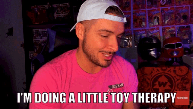 a man wearing a pink shirt and a white hat is saying i 'm doing a little toy therapy