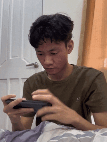 a young man wearing a green shirt with an eagle on it is playing a game on his phone