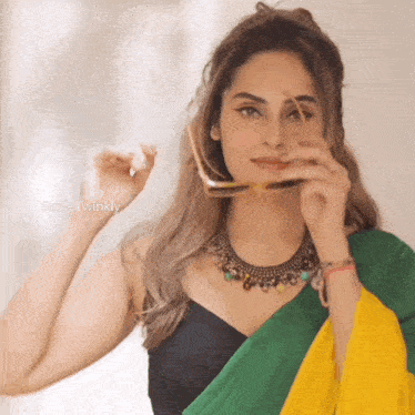 a woman wearing a black top and a green and yellow saree is holding a pair of glasses over her face
