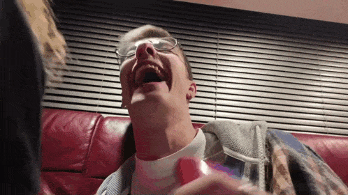 a man with glasses is laughing on a red couch