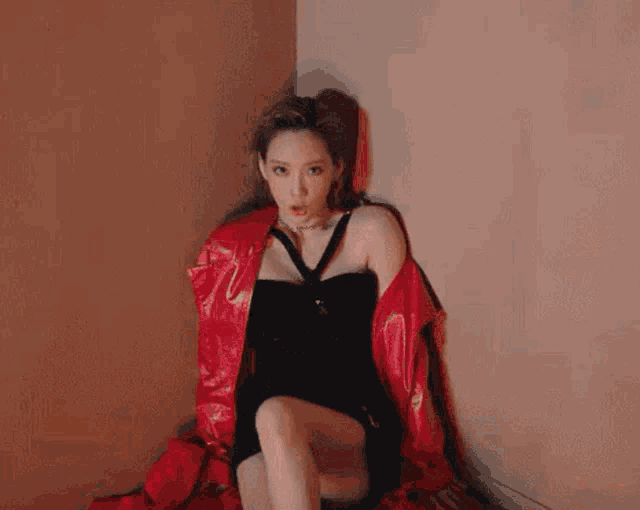 a woman in a black dress and a red jacket is sitting on the floor .