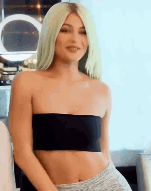 a woman with blonde hair is wearing a black crop top and grey shorts .
