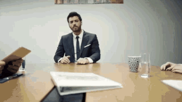a man in a suit and tie is sitting at a table in a meeting room .