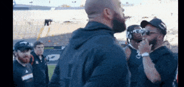 a group of men are standing in a stadium and one of them is wearing sunglasses and headphones .