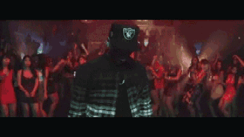 a man wearing a raiders hat is standing in front of a crowd of people dancing