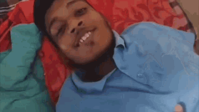 a man in a blue shirt is laying on a bed with his eyes closed .