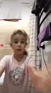 a little girl wearing a pink shirt with a donut on it is standing in a bathroom .
