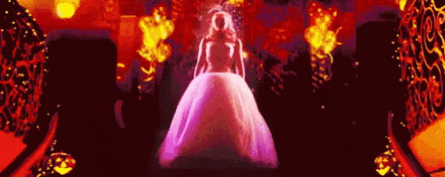 a woman in a long white dress is standing in a dark room surrounded by fire .