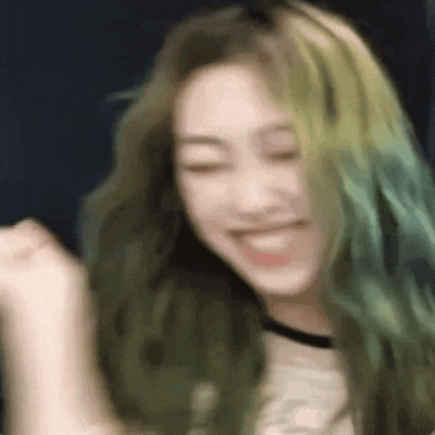 a woman with green hair is smiling with her eyes closed and her hands in the air .