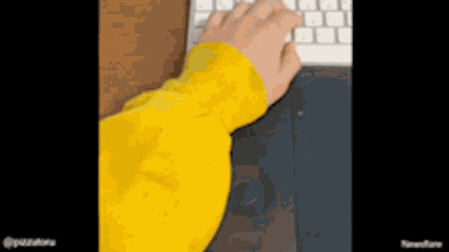 a person in a yellow sweatshirt is typing on a keyboard
