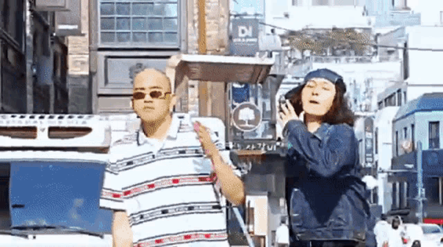 two men are standing next to each other on a city street talking on a cell phone .