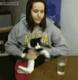 a woman holding a black and white cat while wearing a hoodie that says alberta on it